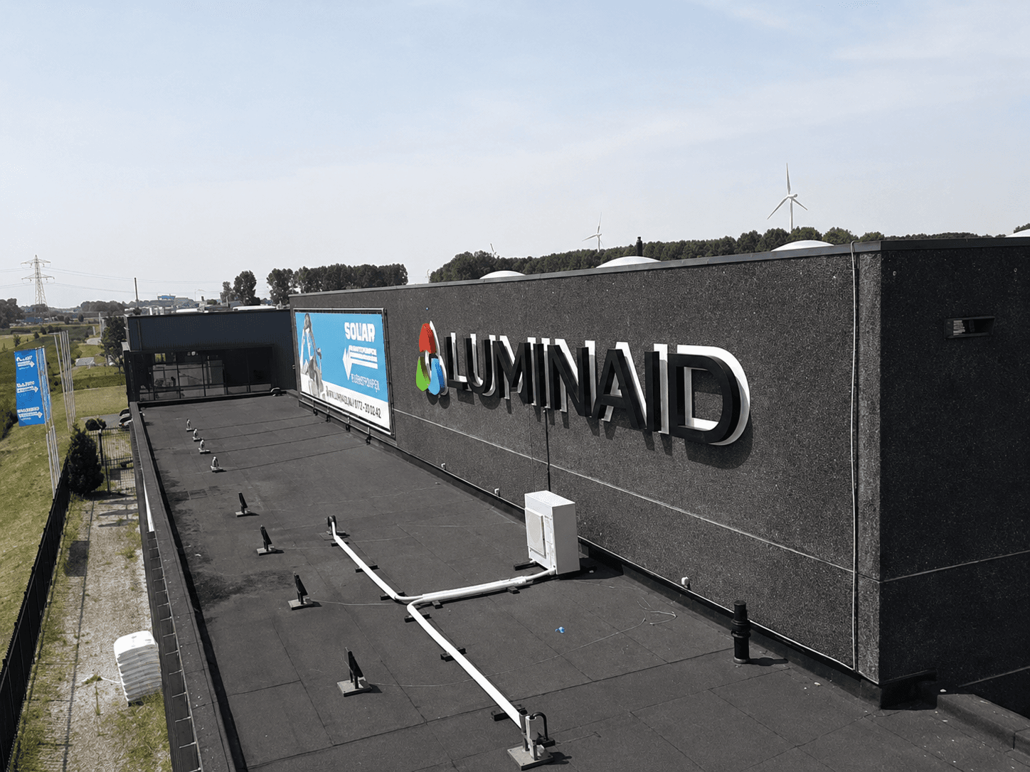 Donkere gevel van een bedrijfspand met gevelreclame van Luminaid, bestaande uit een full-colour logo en witte 3D doosletters langs een plat dak.