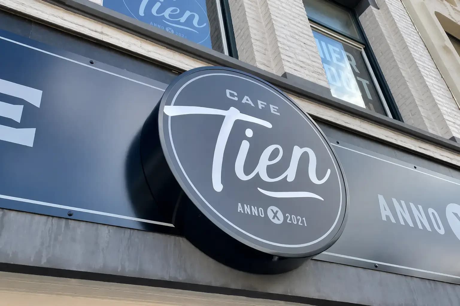 Rond donkerblauw gevelbord van Café Tien met witte belettering en logo, gemonteerd als uithangbord aan de voorgevel van een horecapand.