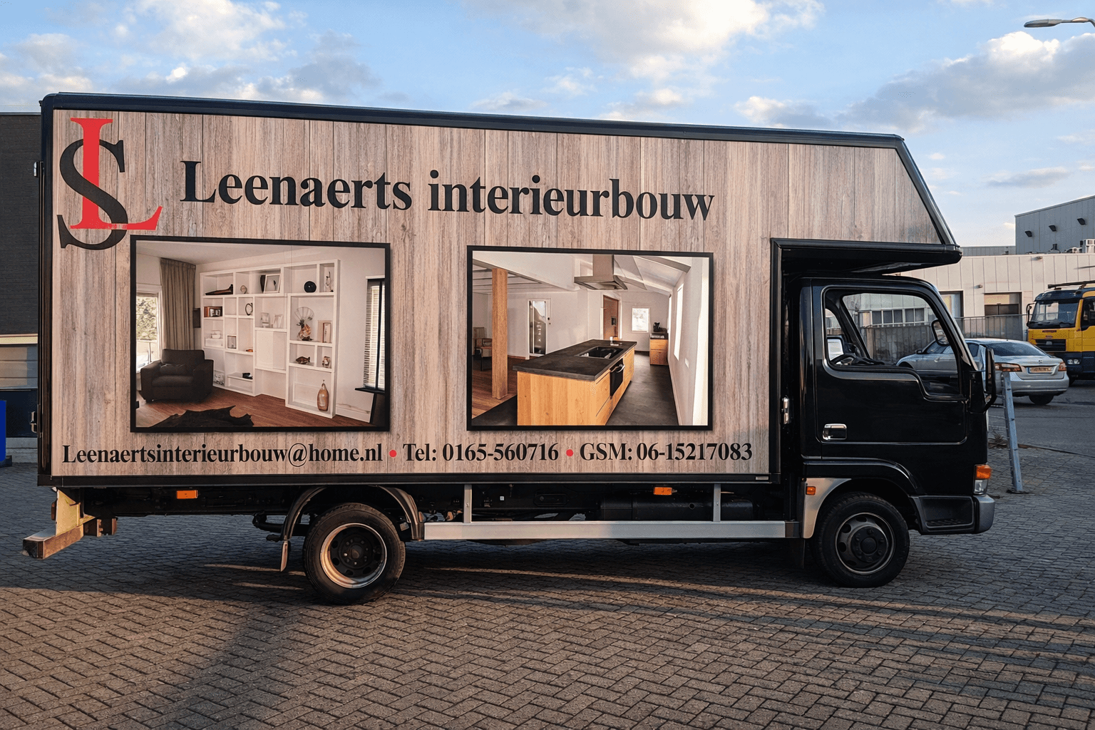 Zwarte bedrijfswagen met full-color voertuigbelettering voor Leenaerts interieurbouw, voorzien van een houtlook wrap, groot logo, zwarte geveltekst en twee interieurfoto’s op de zijwand.