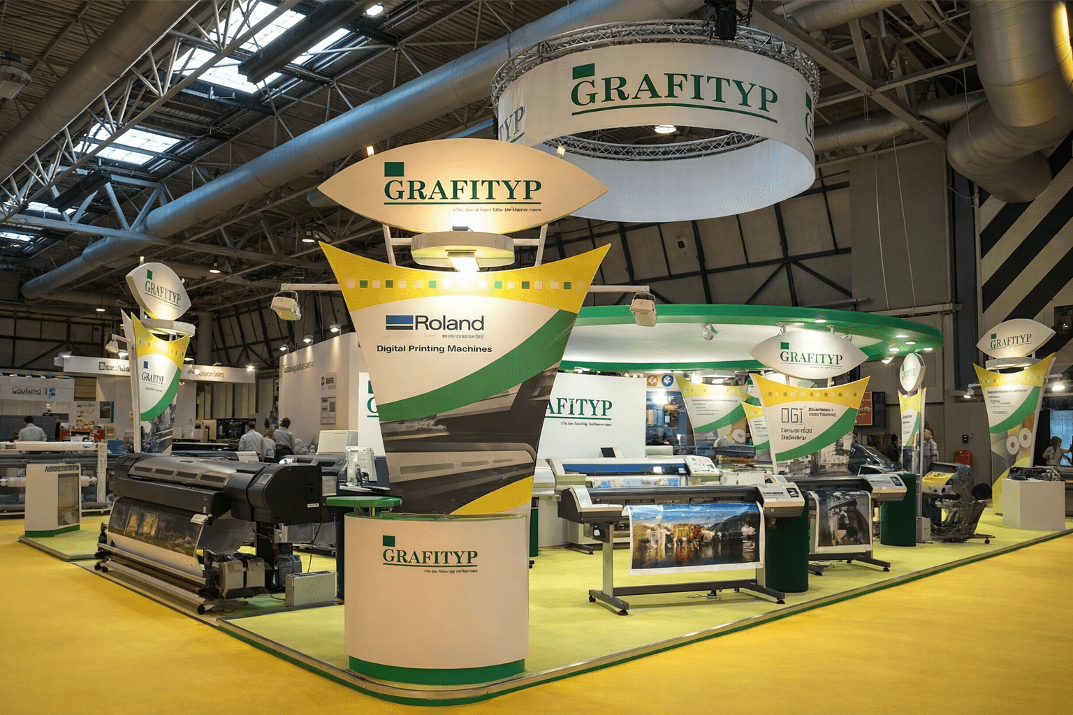 Ruime GRAFITYP-beursstand met hangende logobanner, hoge displayzuilen en grootformaat printers voor digitale printtoepassingen op een vakbeurs.