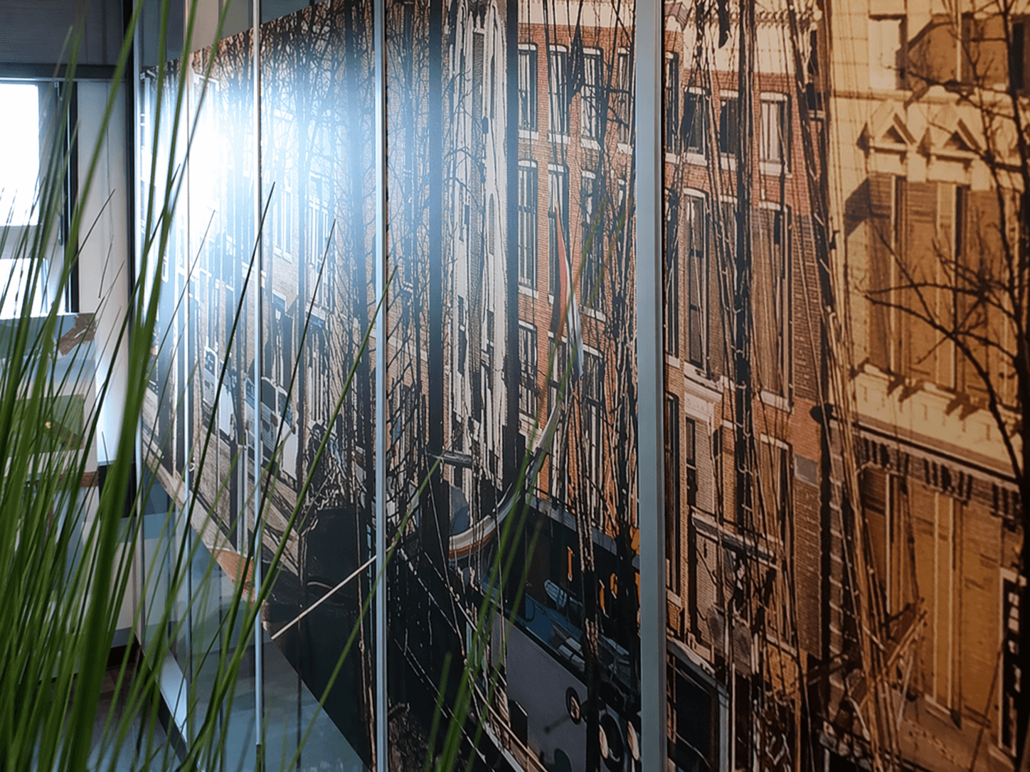 Glazen kantoorwand met full-colour glasfolie van Amsterdamse gevels en grachtenpanden, toegepast als decoratieve privacyfolie in een moderne werkomgeving.
