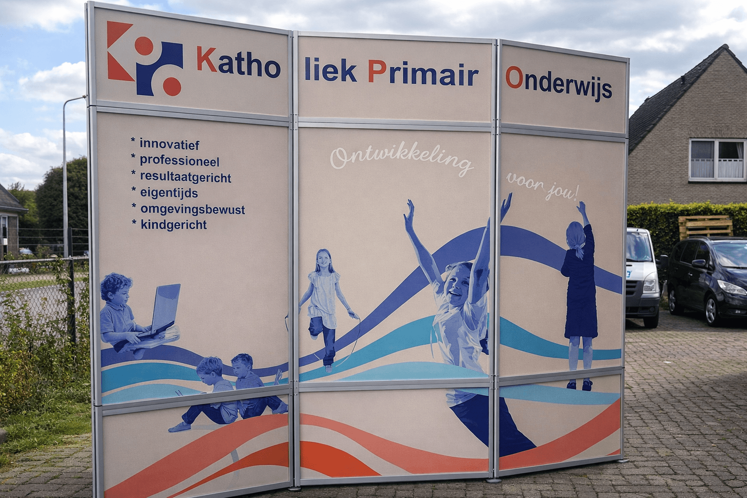 Gebogen buitenbord met full-colour panelen voor Katholiek Primair Onderwijs, met logo, kernwaarden in tekst en blauwe illustraties van spelende kinderen.