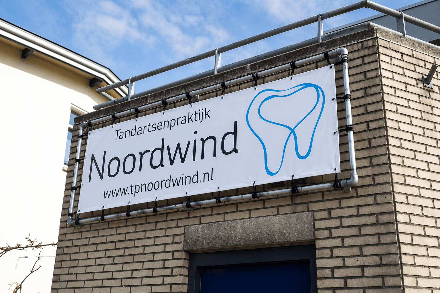 Witte gevelbanner in buizenframe voor Tandartsenpraktijk Noordwind met tandlogo op een bakstenen gevel.
