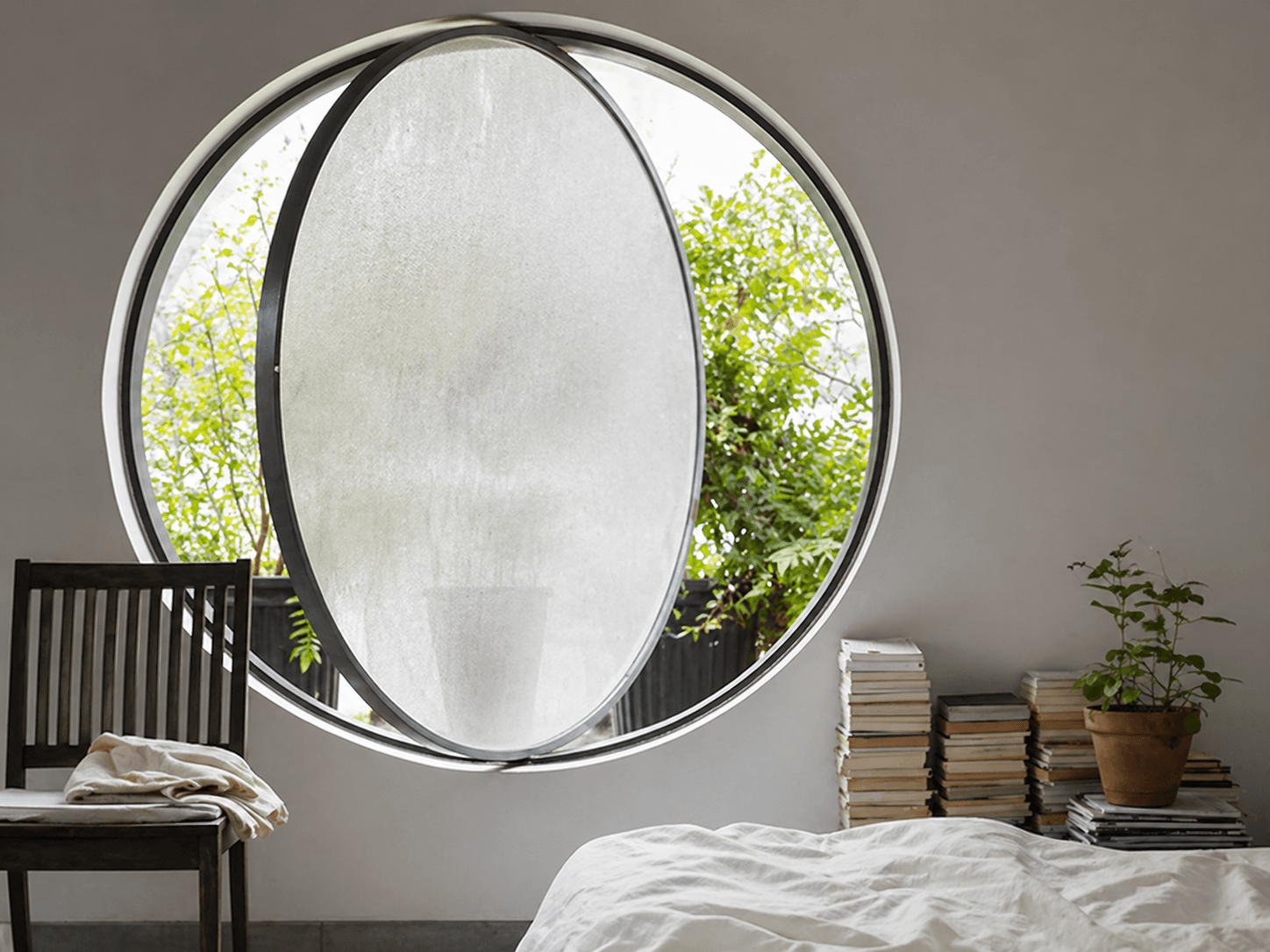Rond raam met matte privacyfolie in een slaapkamer, met zwarte kozijnen en zicht op groen buiten.