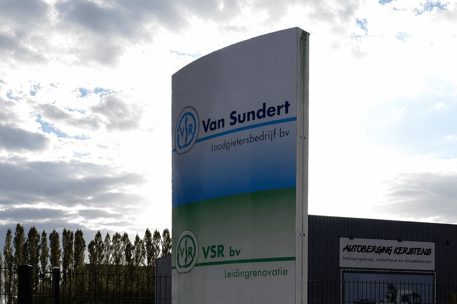 Vrijstaande reclamezuil met Van Sundert Loodgietersbedrijf bv en VSR bv Leidingrenovatie bij een bedrijventerrein.