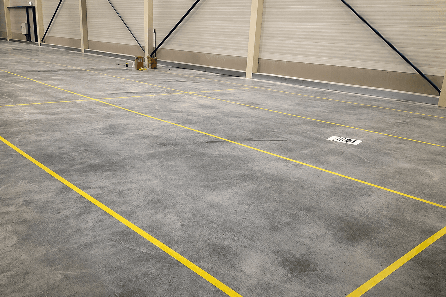 Gele vloermarkering op een betonnen bedrijfsvloer in een magazijnhal, met strakke belijning voor looproutes, werkzones en industriële wayfinding.