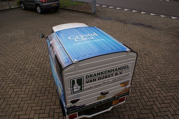 Bovenaanzicht van een compacte bezorgscooter met gesloten laadbak, voorzien van blauwe dakbestickering voor Crystal Clear en achterbelettering van Drankenhandel Van Dorst B.V. op een bedrijventerrein.