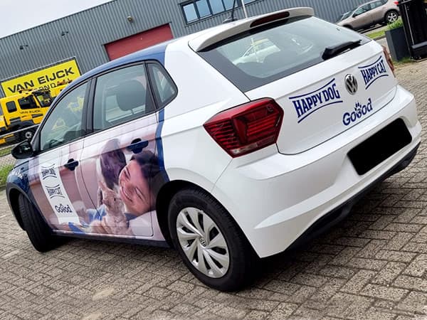 Witte personenauto met full-colour voertuigbelettering voor diervoeding, voorzien van fotoprint op de zijpanelen en merklogo’s op de achterklep op een bedrijventerrein.