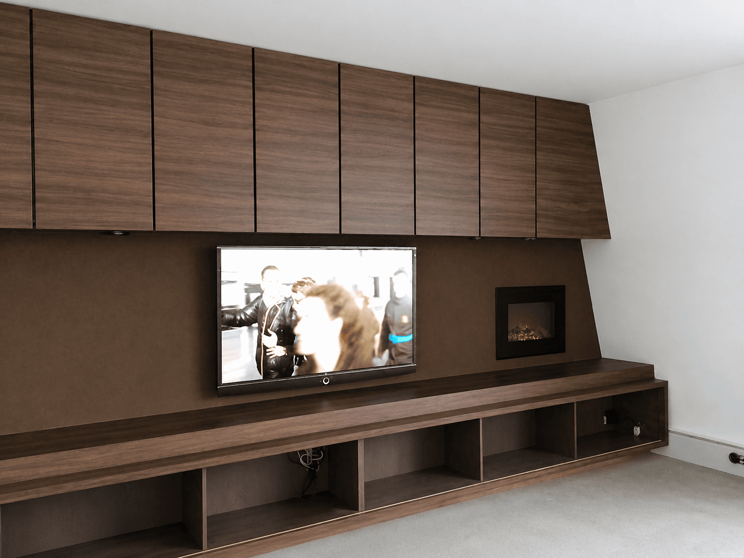 Maatwerk interieurwand met houten wandpanelen, ingebouwde tv en elektrische haard, toegepast als strakke decoratieve wandbekleding in een woonruimte.