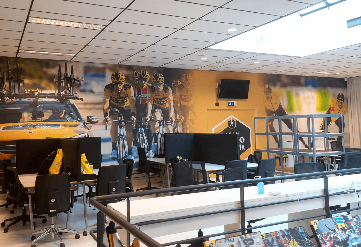 Kantoorruimte met kamerbrede wandprint van Team Jumbo-Visma wielrenners, toegepast als opvallende interieurvisual en decoratieve wandbekleding achter werkplekken.