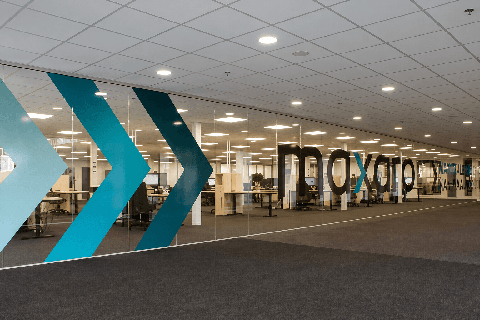 Glaswandbelettering met turquoise pijlen en groot bedrijfslogo op een glazen kantoorwand in een open kantoorruimte.