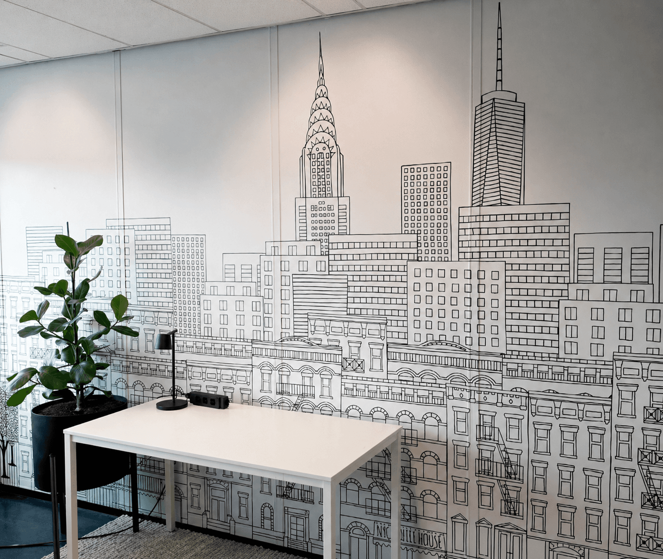 Kantoorruimte met kamerbrede wandprint van een zwart-witte stadsillustratie, toegepast als decoratieve muurvisual en interieurbelettering achter een werkplek.