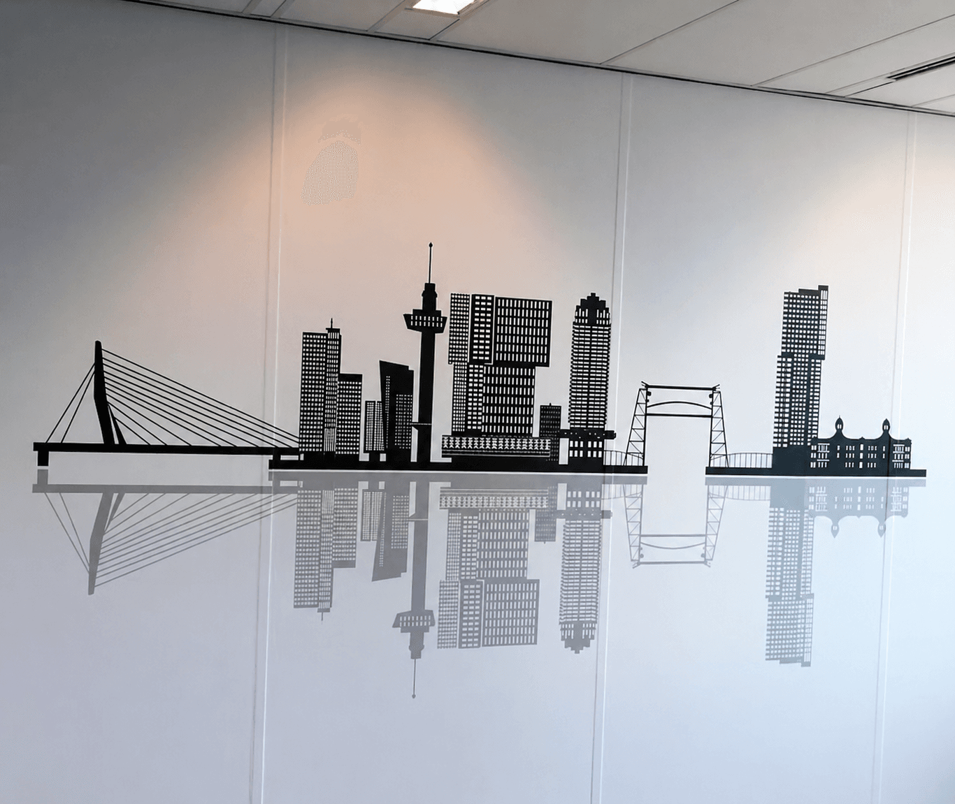 Wanddecoratie met zwarte skyline en spiegeling op een witte binnenmuur, toegepast als minimalistische interieurbelettering en kantoorvisual.